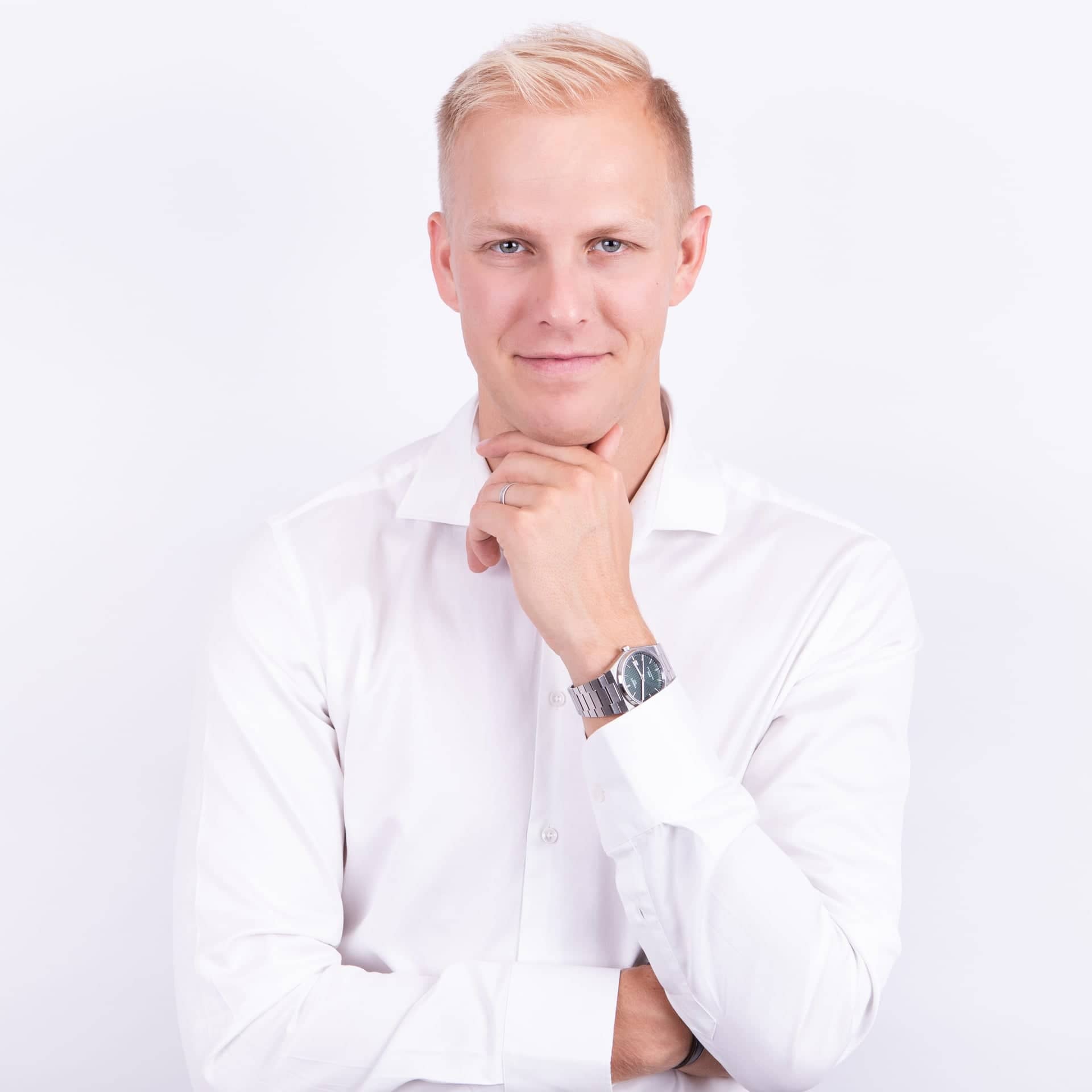 Portrét MUDr. Martina Bortlíka, dermatologa ze Skinity Clinic, oblečeného v bílé košili. Usmívá se a rukou si opírá bradu, působí přátelsky a profesionálně.
