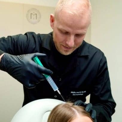 Dermatolog MUDr. Martin Bortlík aplikuje injekci plazmy do vlasové pokožky pacientky při plazmaterapii pro podporu růstu vlasů.